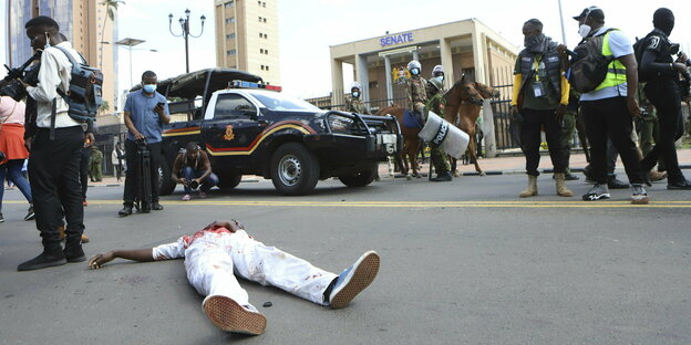 Ein blutender Mensch liegt auf dem Boden, dahinter berittene Polizei und ein Fahrzeug und Passanten