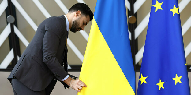 Ein mann im dunklen Anzug richtet die ukrainische und die EU Flagge