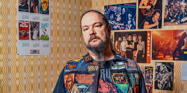 Ernst Lustig mit "Kutte" vor Postern mit Heavy-Metal-Musikern