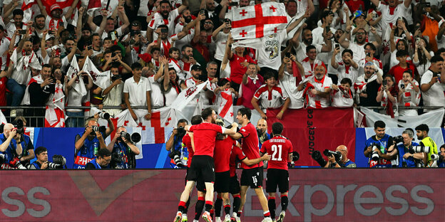 The Georgian players celebrate in a crowd in front of their fan corner