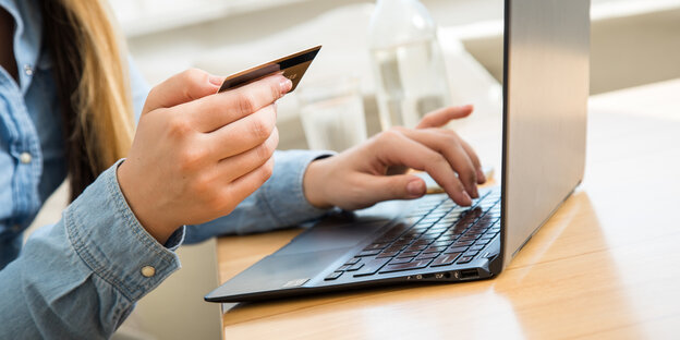 Eine Frau mit Kreditkarte sitzt vor einem Laptop