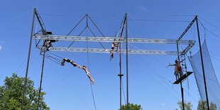 Auf einem Flugtrapez im Volkspark Friedrichshain sind mehrere Menschen an Schaukeln zu sehen und auch, wie sie durch die Luft fliegen