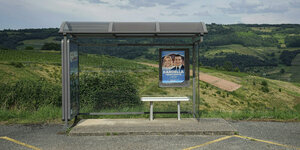 Bushaltestelle mit Wahlplakat von Bardella vor grüner Landschaft