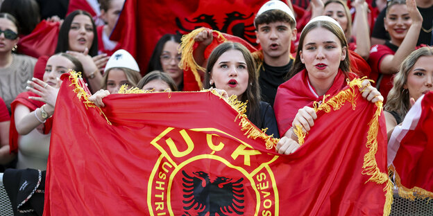Albanische Fans halten eine rote Flagge hoch, auf der UÇK steht