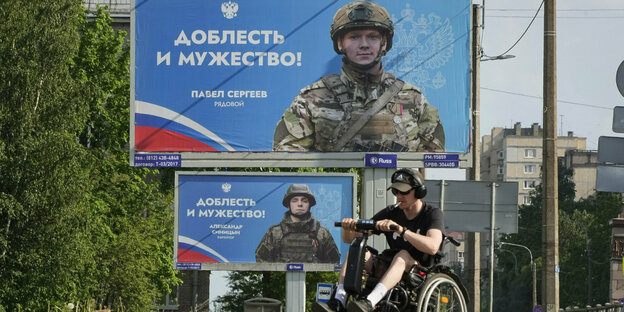 Russische Propgandaplakate und ein Mann im Rollstuhl im Vordergund