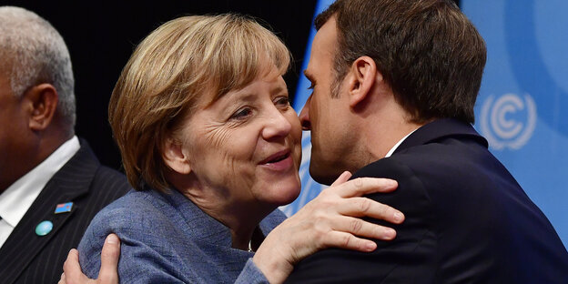 Ex-Bundeskanzlerin, Angela Merkel, und der französische Präsident, Emmanuel Macron, begrüßen sich gerzlich.