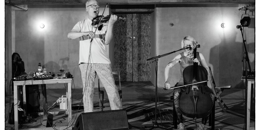 ein Mann spielt stehend Violine, eine Frau sitzend Cello. Beide singen.