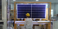 Ein Arbeiter steht in heller Arbeitsklidung vor einem Solarmodul
