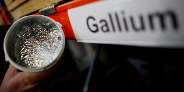 Ein Becher mit silbrig glänzendem Material neben einem Schild, auf dem steht "Gallium"