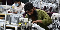 Ein mann sitzt an seinem Arbeitsplatz in einer Textilfabrik und näht mit einer Nähmaschine