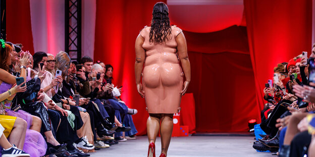 Frau in einer Art "Fatsuit" auf einem Laufsteg