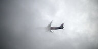 Ein Flugzeug verschwindet halb hinter grauen Wolken, durch die nur ein wenig Licht scheint