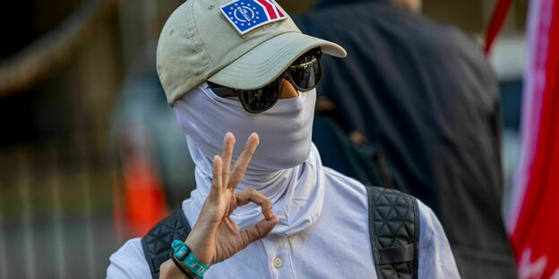 Ein maskierter Mann zeigt mit seinen Fingern das Symbol für "White Power"