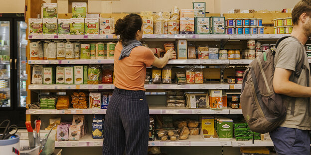 Eine Frau steht an einem Supermarktregal, ein Mann geht vorüber und verschwindet am rechten Bildrand