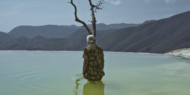 Photo of an old woman with a long gray braid standing in water up to her waist.