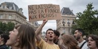 Ein Mann steht in einer Menschenmenge in paris und hält ein Schild in die Höhe