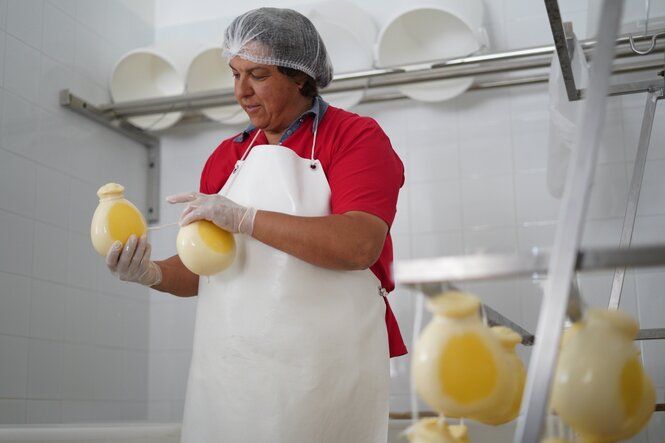 Eine Frau mit Plastikhaube über den Haaren in einer Käserei, sie hält Provola in der Hand