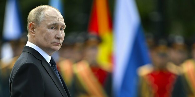 Porträt von Wladimir Putin steht während einer Zeremonie vor Soldaten, die nur unscharft zu erkennen sind