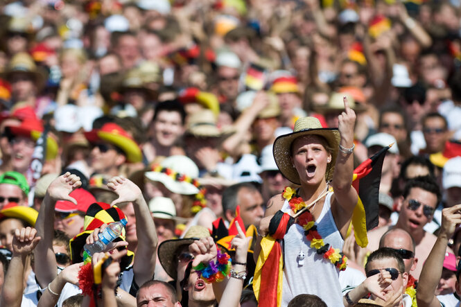 Ein weiblicher Fußballfan mit Nationalflaggenausstattung mit Hut in einem Meer von Fußballfans ruft etwas und hebt den Mittelfinger in die Luft.