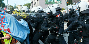 Polizisten mit Helm und Schlagstöcken gehen gegen Demonstrierende vor