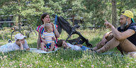 Eine Frau und ein Mann sitzen mit drei kleinen Kindern im Gras