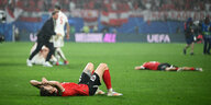 Zwei Fußballspieler in roten Trikots liegen erschöpft und enttäuscht auf dem Rasen