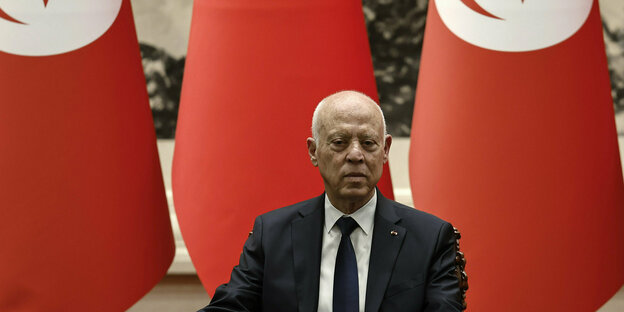 Portät des tunesischen Präsidenten in Anzug mit Krawatte vor roten tunesischen Fahnen
