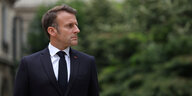 Präsident Emmanuel Macron schaut nach rechts, hinter ihm grünes, unscharfes Buschwerk