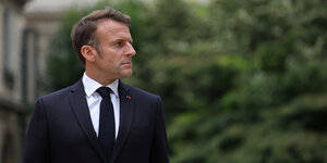Präsident Emmanuel Macron schaut nach rechts, hinter ihm grünes, unscharfes Buschwerk