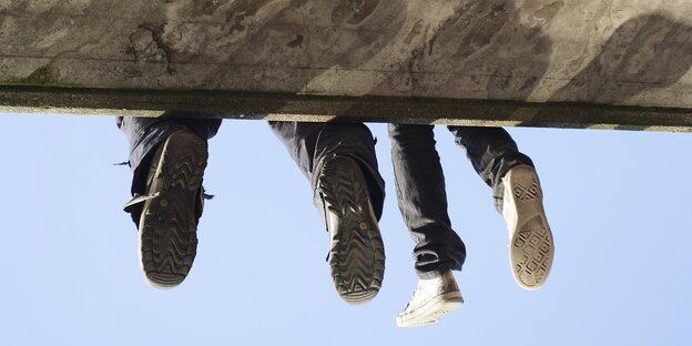 Jugendliche auf Mauer sitzend, Beine baumeln in der Luft
