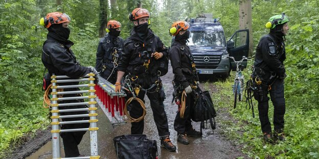 Vermummte Polizisten stehen mit Leitern auf einem Waldweg im Gremberger Wäldchen