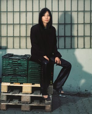 Porträt der Künstlerin Sung Tieu, die auf einem Stapel Kisten sitzt