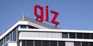 Das rote Logo der Entwicklungsorganisation GIZ ist auf dem Dach eines ihrer Hauptgebäude vor blauem Himmel zu sehen.