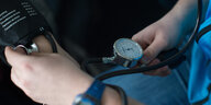 Ein junger Mensch misst bei einem Patienten den Blutdruck.