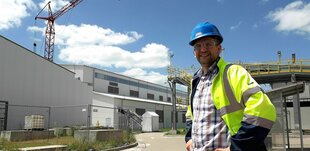 Mann mit Helm und Signaljacke auf einem Werksgelände