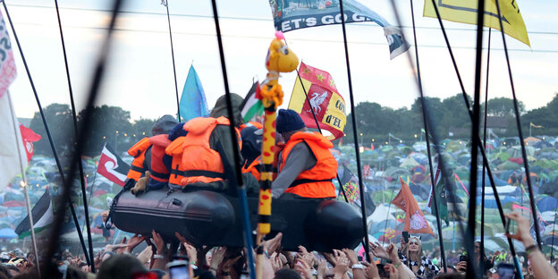 Ein Schlauchboot von Banksy wird von der Menge auf Händen getragen beim Glastonbury Musikfestival