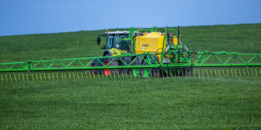 Ein Traktor zieht eine Spritze mit breiten Auslegern und verteilt Dünger