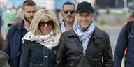 Emmanuel Macron und seinFrau Brigitte Macron gehen, begleitet von verschiedenen Männern, am Strand spazieren. Macron trägt eine Lederjacke