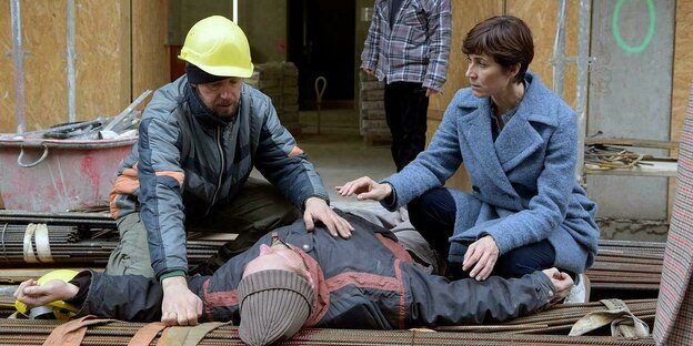 Ein Bauarbeiter und eine Frau knien vor einem Mann, der auf dem Rücken liegt