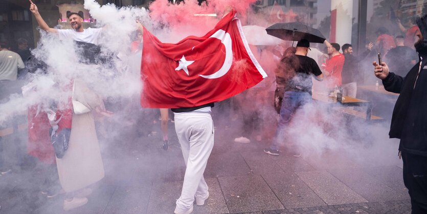 Menschen auf dem Gehsteig in Feierlaune, einer hält eine Türkei-Flagge hoch.