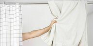 Ein Mann greift hinter dem Duschvorhang nach einem Handtuch, das über der Stange hängt