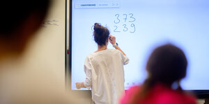 eine Person schreibt Zahlen auf ein Whiteboard in einem Klassenraum