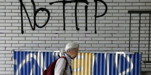 Eine ältere Frau geht an einem Graffiti "No TTIP" vorbei.