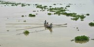 Dorfbewohner fahren in einem Boot durch ein überflutetes Dorf im Distrikt Morigaon
