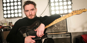 Felix Brückner sitzt mit einer Gitarre in einem fensterlosen Raum