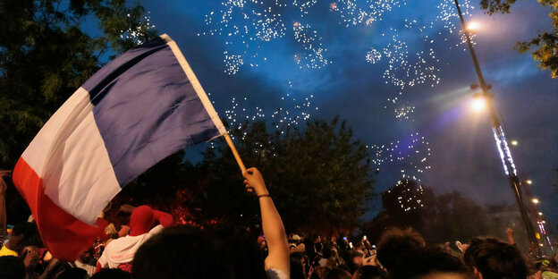 Feiernde mit französicher Trikolore und Feuerwerk auf nächtlicher Straße