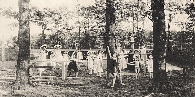 Eine historische Aufnahme zeigt winkende Frauen und Kinder unter Bäumen.