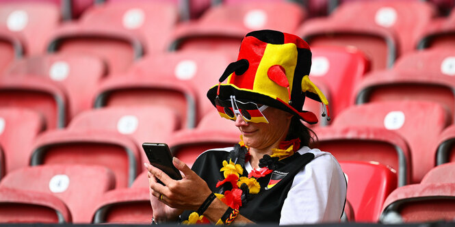 Eine Person in schwarz-rot-gold Vollmontur auf der leeren Stadiontribüne