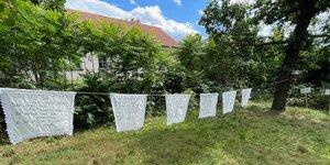 Gestickte Poesie weht auf einer Wäscheleine auf einer Wiese unter Bäumen sachte im Wind auf einem Friedhof in Friedrichshain: Sascha Lyamina arbeitet mit meditativen Formen