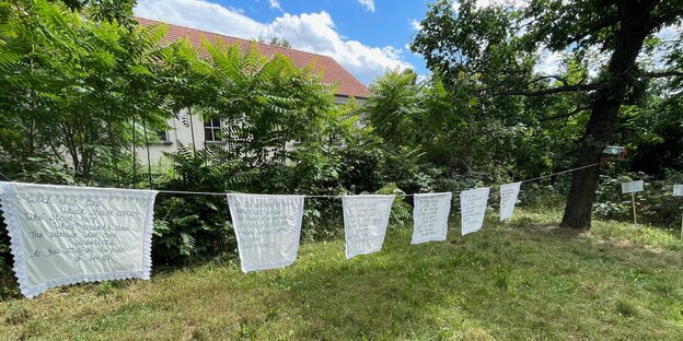 Gestickte Poesie weht auf einer Wäscheleine auf einer Wiese unter Bäumen sachte im Wind auf einem Friedhof in Friedrichshain: Sascha Lyamina arbeitet mit meditativen Formen